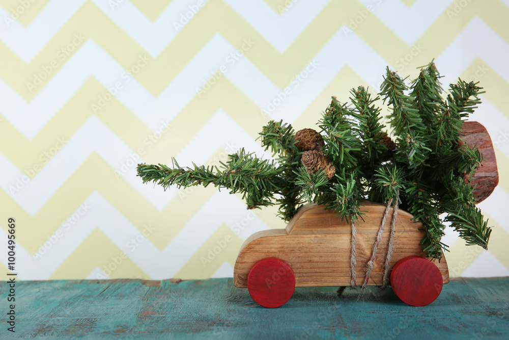 Wooden toy car with Christmas tree on a table over pattern background