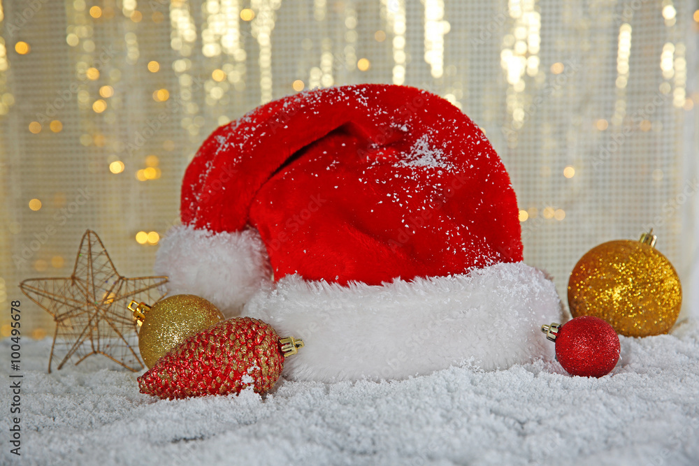 Santa Claus hat with toys on a snowy table over glitter background