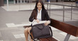 © Dash - Attractive stylish young businesswoman sitting on a wooden urban bench placing her laptop in a bag with a smile