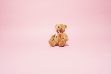 vintage brown teddy bear with bow against pink background.
