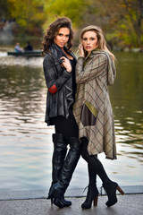 Wall Mural - Two elegant fashion models posing in the autumn park against the lake.