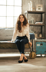 smiling brunet woman in elegant clothing sitting in loft room