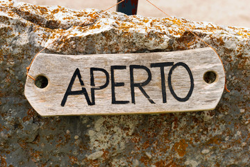 Aperto - Open Sign in Italian Language / Wooden rustic sign with text Aperto (open in italian language). Hanging with a rope on a rock