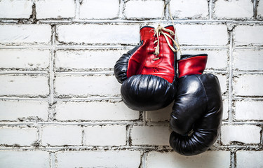 A pair of old boxing gloves hanging on white brick wall background.