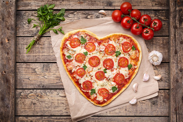 Valentines day heart shaped pizza margherita vegetarian love concept with mozzarella. tomatoes, parsley and garlic on vintage wooden table background.