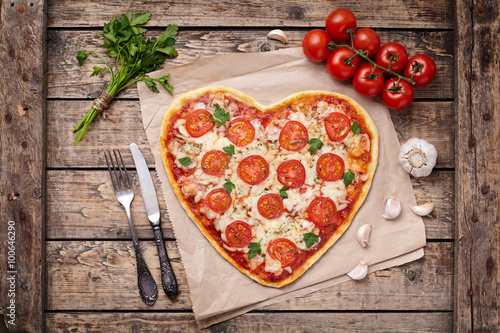 Nowoczesny obraz na płótnie Heart shaped pizza margherita love concept for Valentines Day with mozzarella, tomatoes, parsley and garlic on vintage wooden table background.