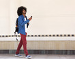 © mimagephotos - Smiling young black man walking with bag and mobile phone