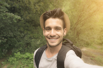 Handsome guy is taking a selfie with his smartphone in the nature - people, technology and lifestle concept