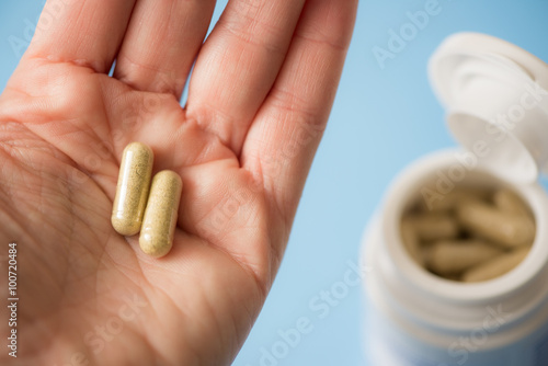 Fotografia Twice-a-day : hand holding two capsules, medicine bottle in background