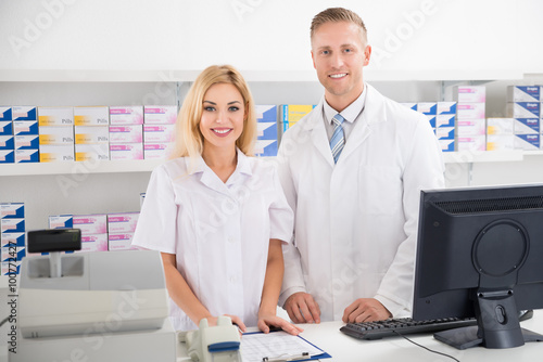 Fotografering Pharmacists Smiling At Counter In Pharmacy