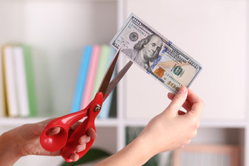 Poster - Hands with scissors cutting dollar banknote, on blurred interior background