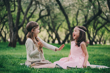 happy little girlfriends playing together in spring park. Dressy sisters having fun outdoor on the warm cozy walk. Friendship concept.