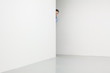 Man in white room looking from behind corner