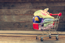 Shopping Cart With Clothing And Baby Pacifiers On The Old Wood Background. Toned Image.