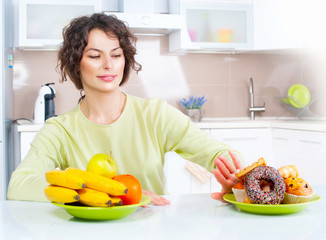 Wall Mural - Dieting concept. Beautiful young woman choosing between fruits and sweets