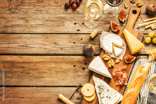 Cuadros en Lienzo Different kinds of cheeses, wine, baguettes, fruits and snacks on rustic wooden table from above