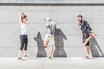 Wall Mural - On a sunny day, a three friends in sportswear does stretching outdoors near a building