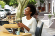 © mimagephotos - Young african woman laughing with mobile phone at cafe