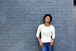 © mimagephotos - Cheerful young black woman standing against gray wall