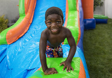 Smiling Little Boy Sliding Down An Inflatable Bounce House