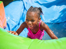 Smiling Little Girl Playing Outdoors On An Inflatable Bounce House Water Slide
