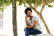 © mimagephotos - African woman relaxing on a bench and using cell phone
