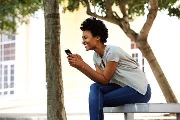 Wall Mural - Cheerful young woman sitting on a bench reading text message