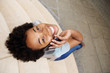 © mimagephotos - Smiling young african woman looking up and using mobile phone
