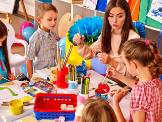 Wall Mural - Children with adult beautiful teacher woman painting and craft  on paper in kindergarten . 