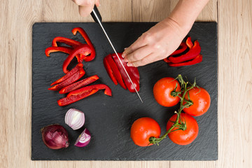 Top down view on cutting board with hands slicing vegetables