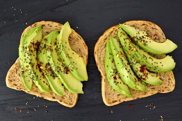 Wall Mural - Open avocado sandwiches with chia seeds on whole grain bread against a dark slate background