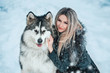 beautiful woman in a fur coat walks in the winter snow-covered wood, lady and a huge fluffy husky walk in nature in December in anticipation of Christmas,luxury dog-wolf,fashionable toning