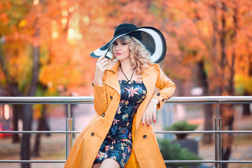 Beautiful stylish woman in a yellow coat and hat with long walks through fields autumn city,business women,lady in the city,creative computer colors,fashionable toning