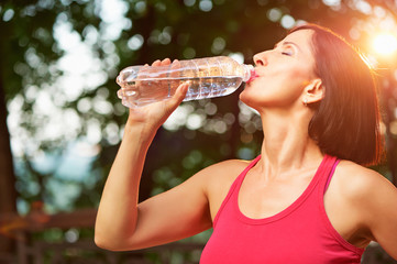 Senior athletic woman drinks water from a bottle after running i