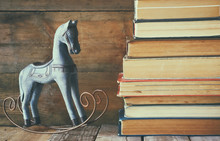 Stack Of Old Books Next To Decorative Rocking Horse Wooden Table. Vintage Filtered Image
