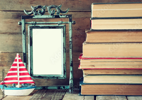 Stack Of Old Books Next To Decorative Sailing Boat And Blank Frame
