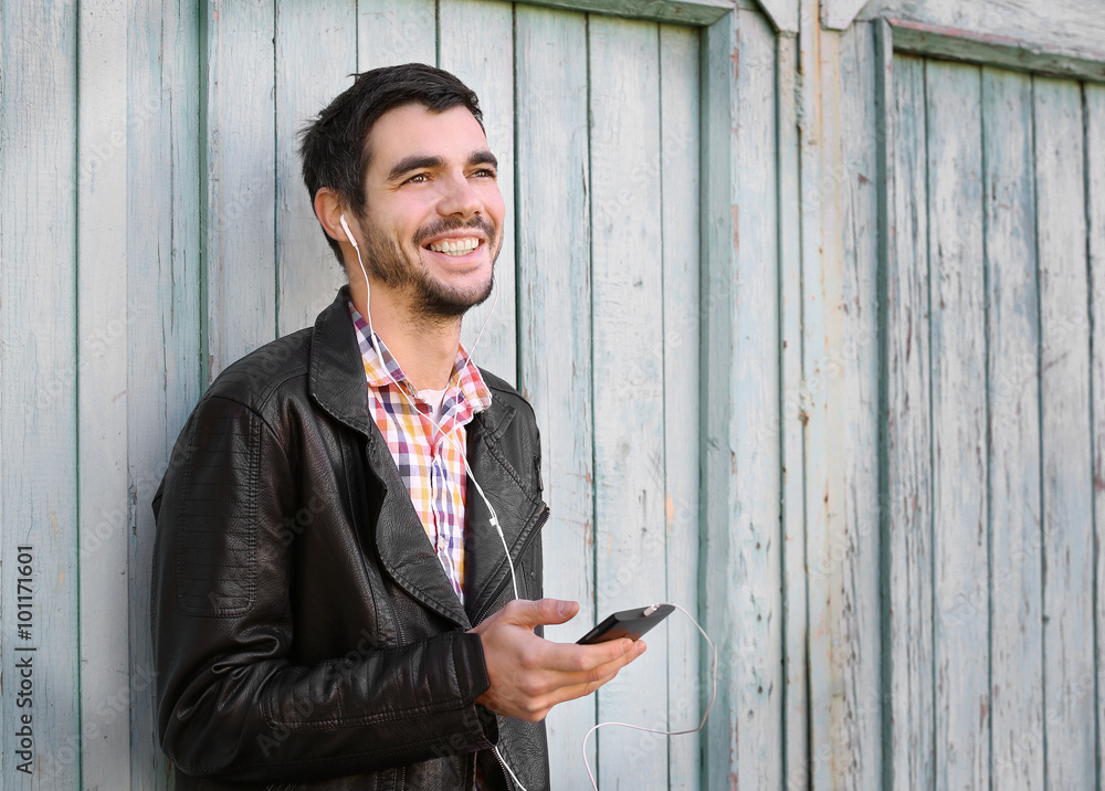 Young man listening to music on a house wall background