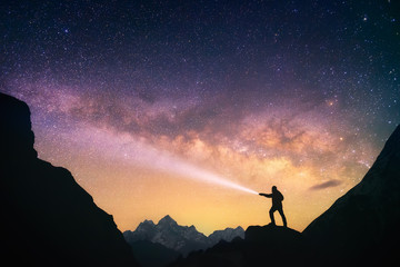 Wall Mural - silhouette of the man standing against the milky way in the mountains with a flashlight in his hands