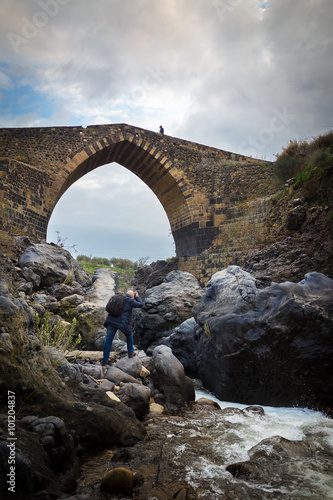 Fotografia, Obraz Photographer taking a photo to a man walking on the "Bridge of Saracens": an old