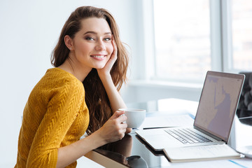 Canvas Print - Woman sitting at the table with laptop and drinking tea