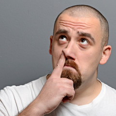 Wall Mural - Portrait of a man putting finger in his nose against gray backgr