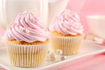 Canvas Print - Two tasty pink cupcakes and teapot, closeup