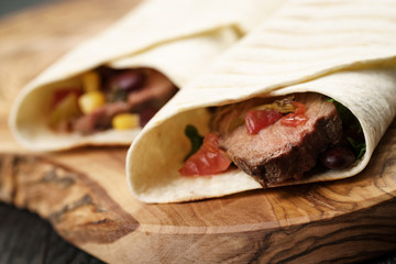 burritos with beef steak, corn, black beans and salsa sauce on cutting board