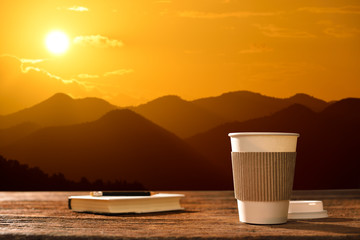 Wall Mural - Paper cup of coffee with mountain background at sunrise
