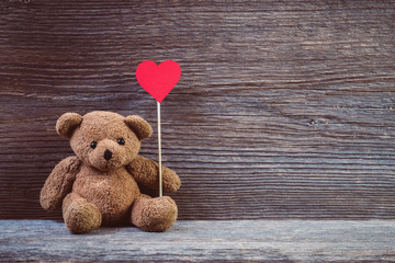 teddy bear with heart sitting on old wood background.