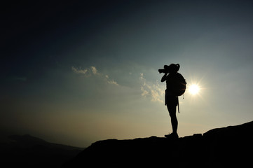 Wall Mural - woman photographer taking photo on sunset mountain peak