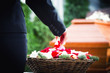 Frau auf Beerdigung streut Rosenblätter auf Sarg