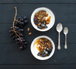 Healthy breakfast set. Bowls of oat granola with yogurt, fresh grapes, almond and  honey over black wooden backdrop