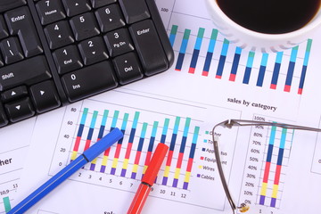 Pen, glasses, computer keyboard and cup of coffee on financial graph, business concept