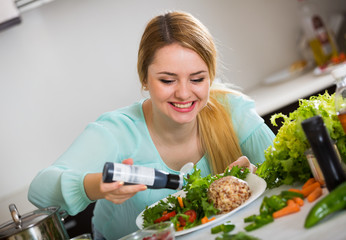 Wall Mural - Cheerful girl in blouse adding sauce in salad with cheese